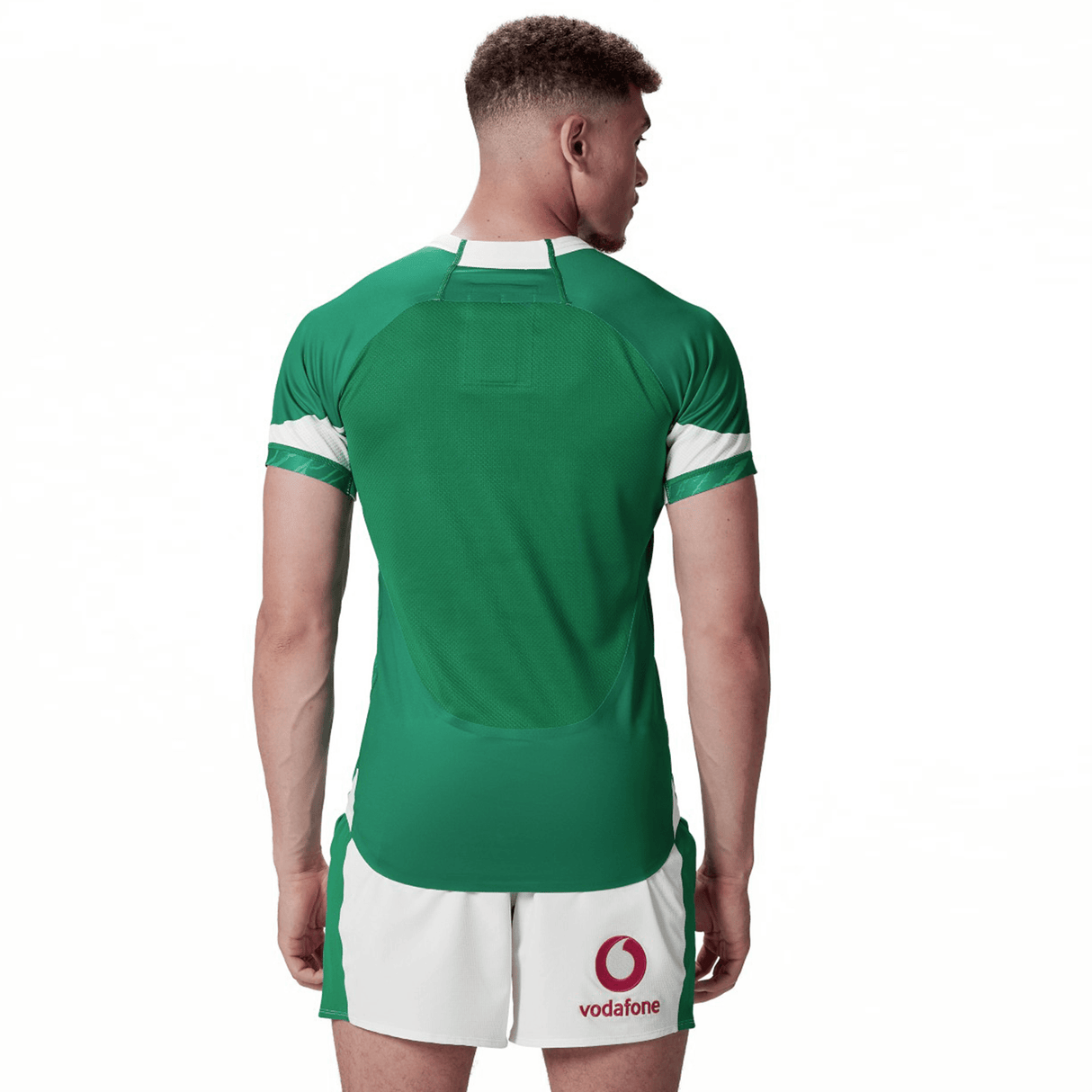 A male athlete in a green and white Ireland 24 Home Test Jersey by Canterbury, featuring a Vodafone logo on the shorts, stands facing away from the camera, highlighting its performance fit designed by Canterbury.