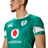 A person wearing a green Ireland 24 Home Test Jersey by Canterbury, complete with IRFU and Vodafone logos and a white and green collar. The VapoDri technology from Canterbury ensures a performance fit.
