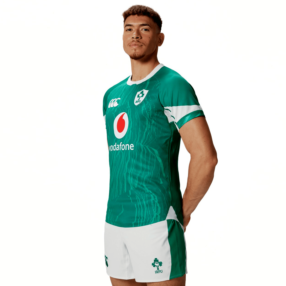 A person in the green and white Ireland 24 Home Test Jersey by Canterbury rugby attire stands with hands by their sides on a plain background, sporting the classic Canterbury gear.