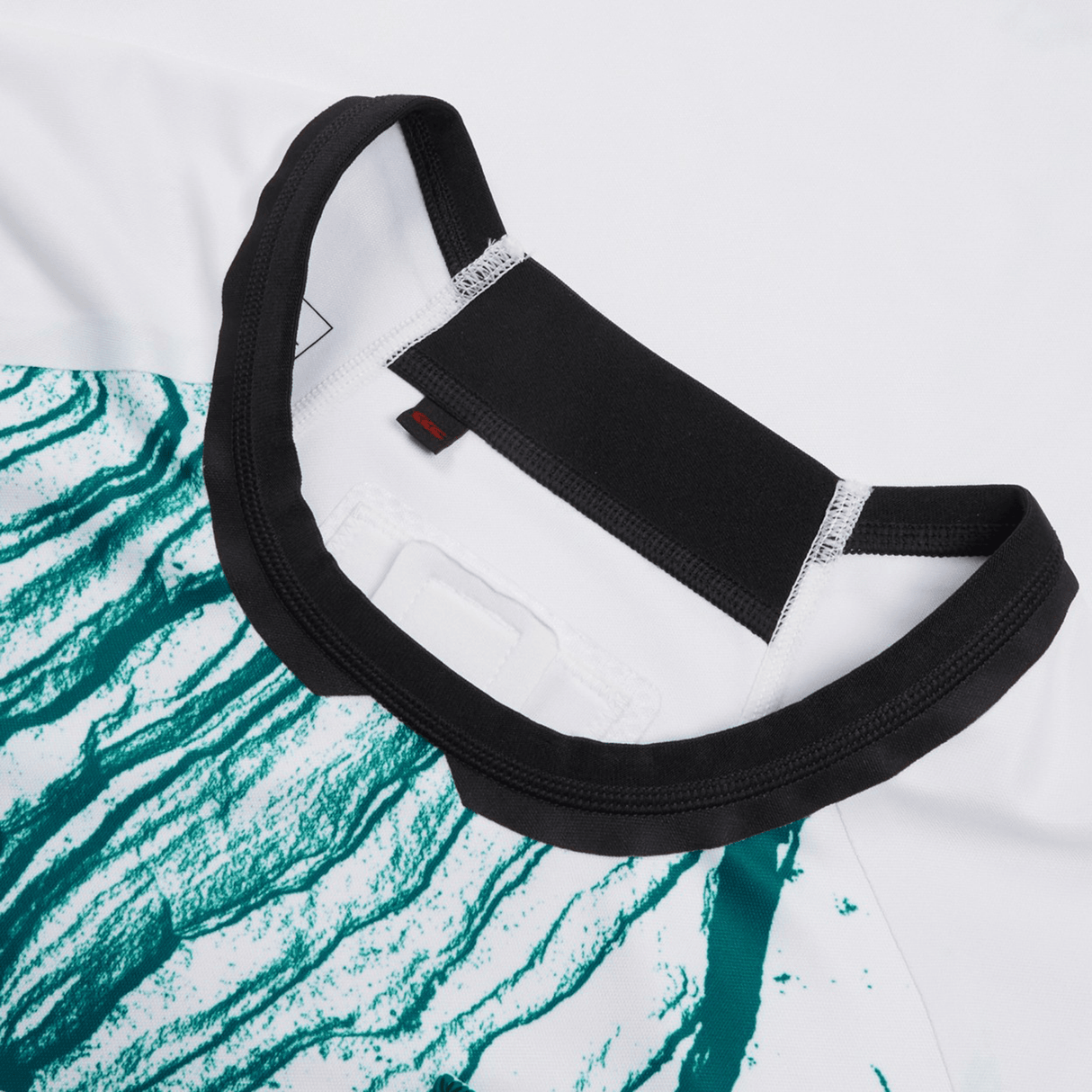 Close-up view of the Ireland 24 Alternate Test Jersey by Canterbury, showcasing a white and teal pattern with a black collar. This VapoDri sports shirt from Canterbury boasts a super slim fit for enhanced performance.