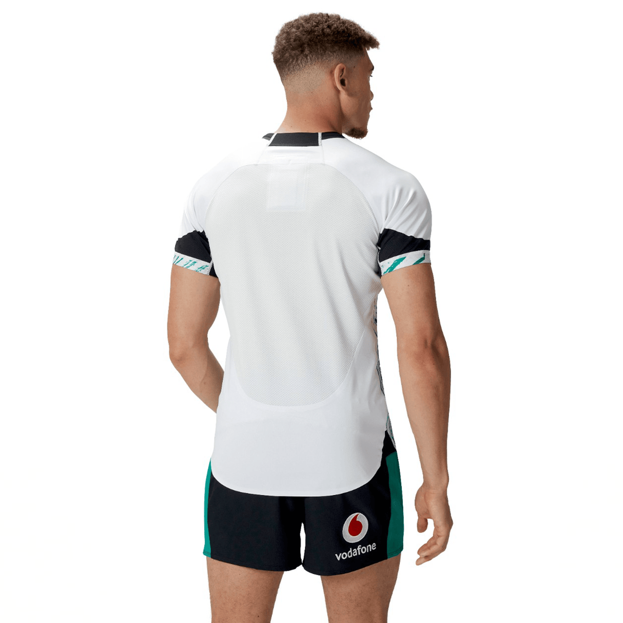 A person stands with their back to the camera, wearing a white and black Ireland 24 Alternate Test Jersey by Canterbury and black super slim fit shorts with green accents. The Vodafone logo is visible on the shorts.