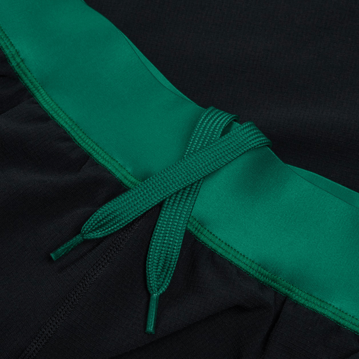 Close-up of the Ireland 24 Alternate Match Short by Canterbury, featuring black athletic shorts with a green waistband and a green drawstring tie at the center, made from durable stretch ripstop fabric.
