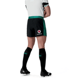 A person wearing a white shirt, Ireland 24 Alternate Match Short by Canterbury featuring a Vodafone logo, black socks, and black cleats stands with hands behind their back.