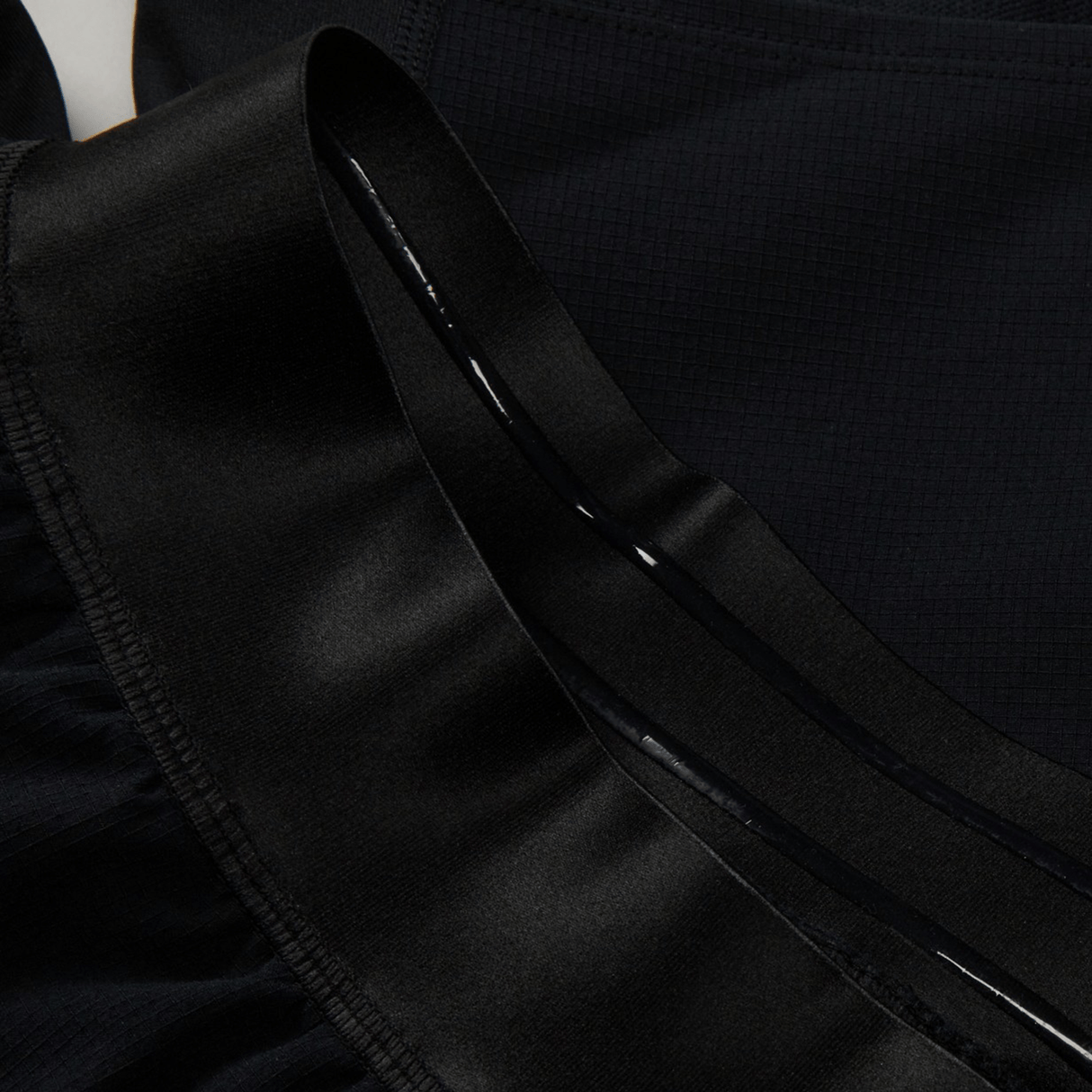 Close-up of a black garment featuring shiny, ruffled fabric and a smooth, satin-like ribbon detail, reminiscent of the premium quality found in the Ireland 24 Training Short by Canterbury.