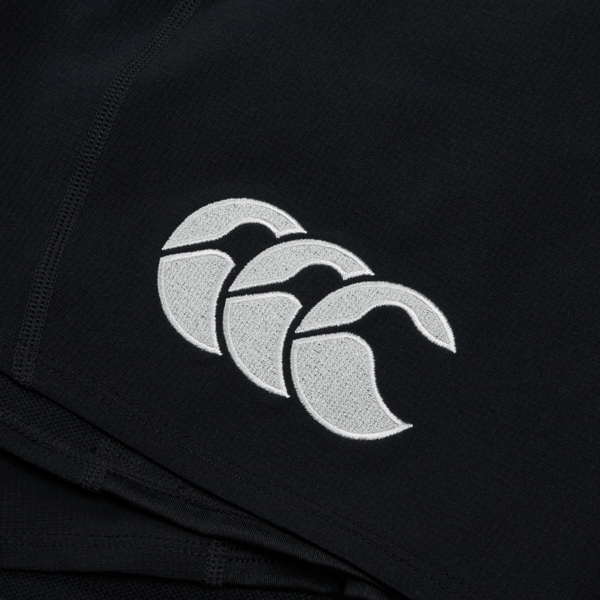 Close-up of a black fabric Ireland 24 Training Short by Canterbury, featuring a white embroidered logo with three overlapping stylized tongues.