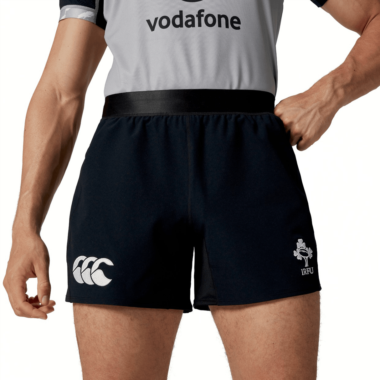 A person is wearing the Ireland 24 Training Short by Canterbury, featuring a black design with a white logo on the left leg and another emblem on the right. They are also donning a grey and black top, epitomizing ideal training apparel.