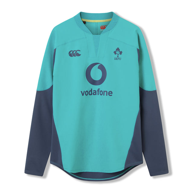 The Ireland 26 Tech Drill Top by Canterbury is a long-sleeved rugby jersey in teal and navy, inspired by IRFU training wear, with the Vodafone logo and IRFU crest on the chest, shown against a plain white background.