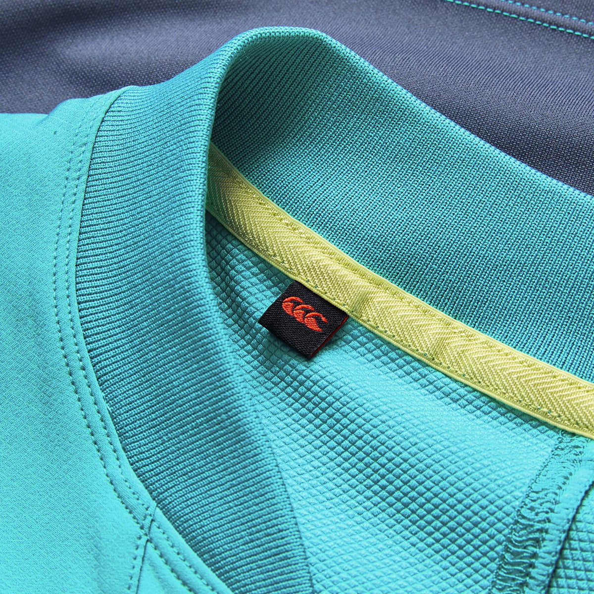 Close-up of the teal collar on the Ireland 26 Tech Drill Top by Canterbury, featuring a yellow inner lining and a black tag with a red logo—showcasing the premium design characteristic of Canterbury’s IRFU training wear.