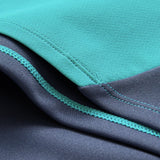 Close-up of two pieces of fabric, one teal and one dark blue, sewn together with visible stitching and seams, featuring details characteristic of the Ireland 26 Tech Drill Top by Canterbury.