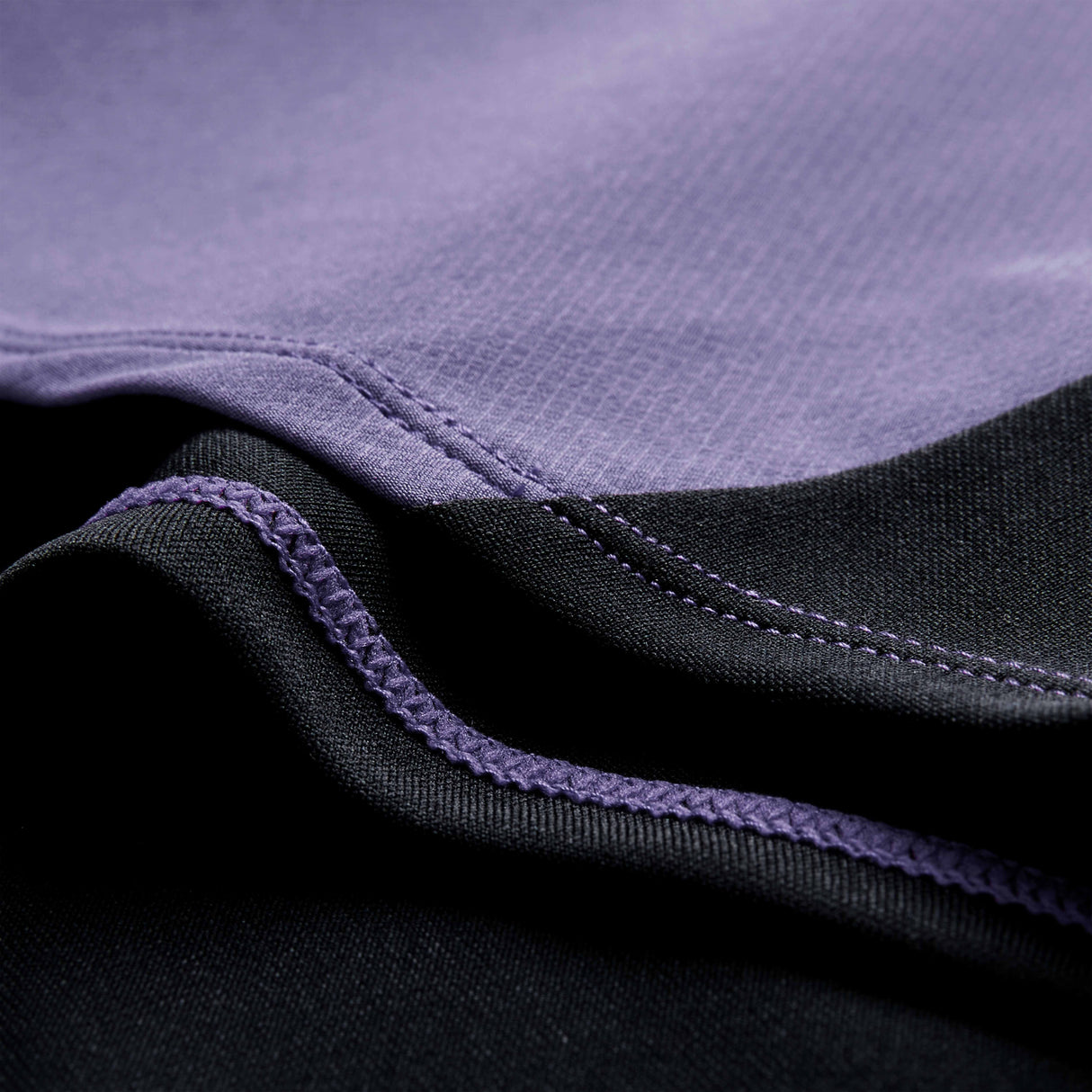 Close-up of fabric with black and purple sections, showing detailed stitching where the two colors meet—typical of premium training wear like the Ireland 26 Tech Drill Top by Canterbury.