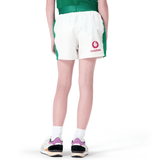 A person stands in a green shirt paired with Junior Ireland 24 Home Match Shorts by Canterbury, crafted from moisture-wicking fabric and featuring the "Vodafone" logo. Wearing sneakers with pink and black accents, they face away.
