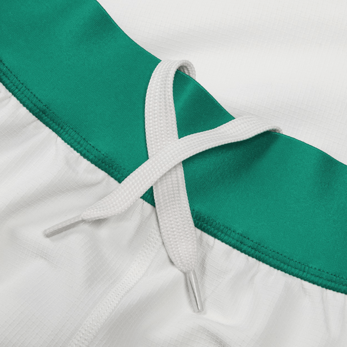Close-up of a white drawstring bow tied on green and white fabric, likely part of moisture-wicking athletic shorts reminiscent of Junior Ireland 24 Home Match Short by Canterbury.