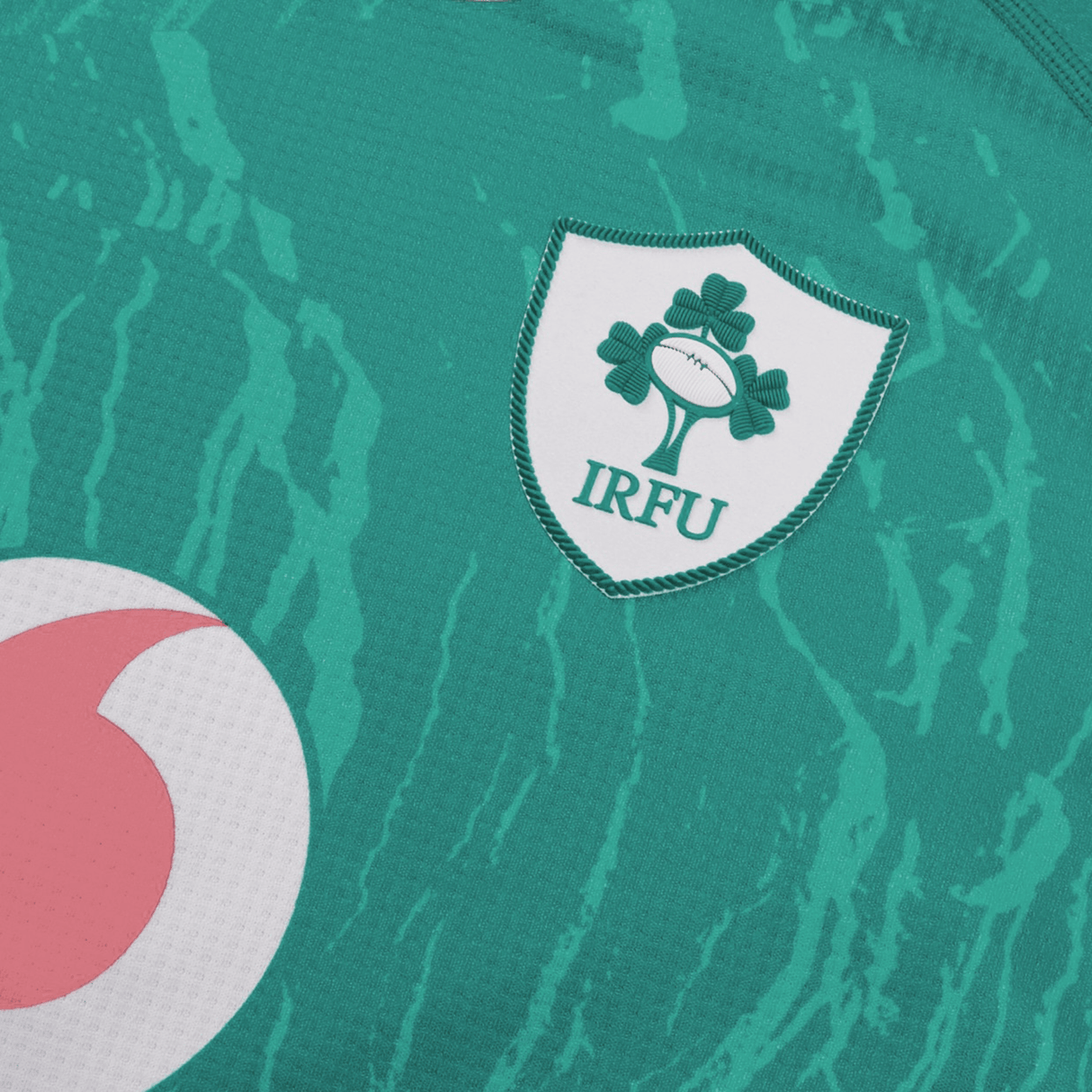 Close-up of the Women's Ireland 24 Home Pro Jersey by Canterbury, featuring the iconic IRFU logo with three shamrocks and a rugby ball, plus a touch of a pink and white emblem. Made with VapoDri technology, this jersey ensures comfort and performance for Ireland Women's Rugby.