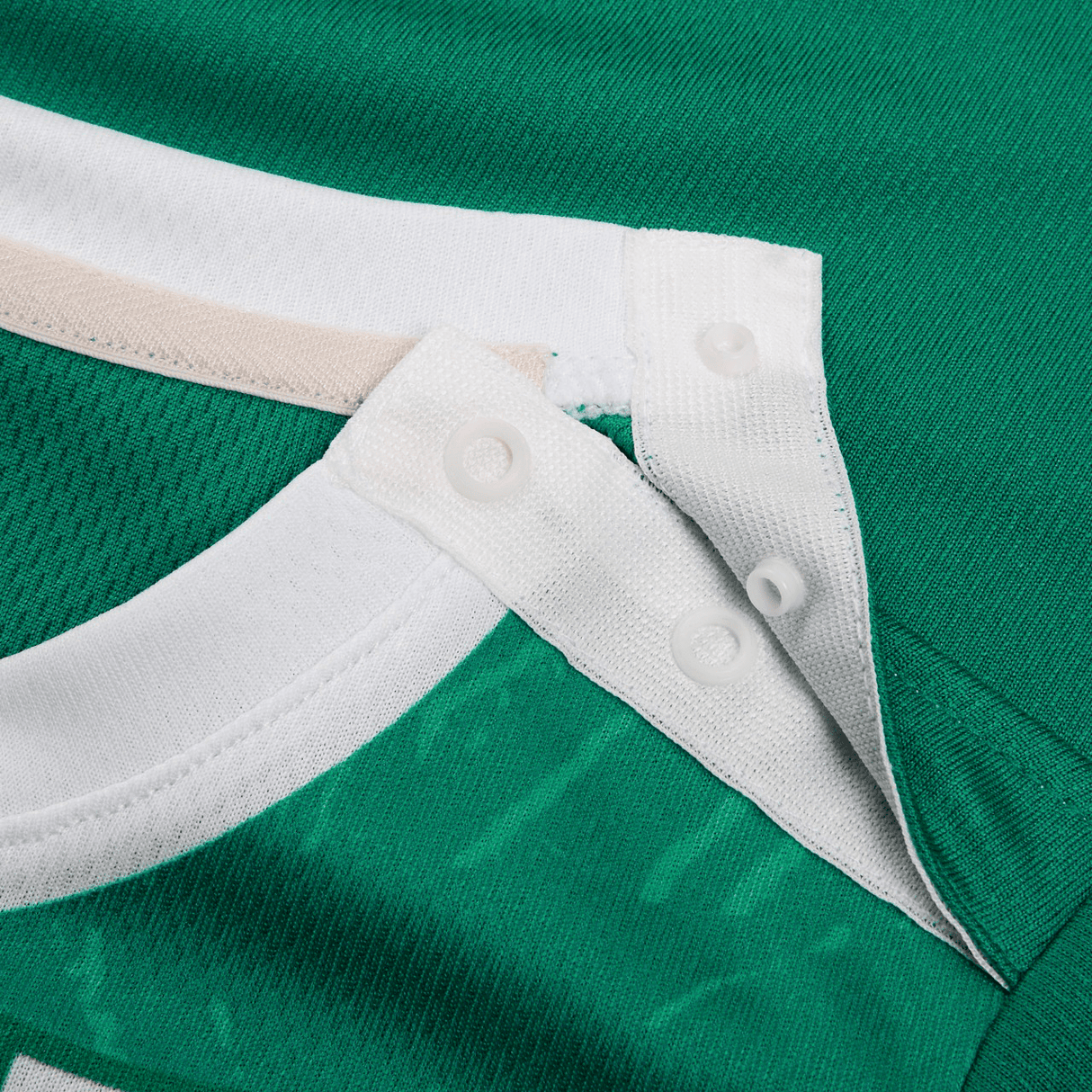 Close-up of a Canterbury green sports jersey from the Infant Ireland 24 Home Pack, featuring snap buttons on a white collar and a contrasting beige strip.