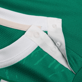 Close-up of a Canterbury green sports jersey from the Infant Ireland 24 Home Pack, featuring snap buttons on a white collar and a contrasting beige strip.
