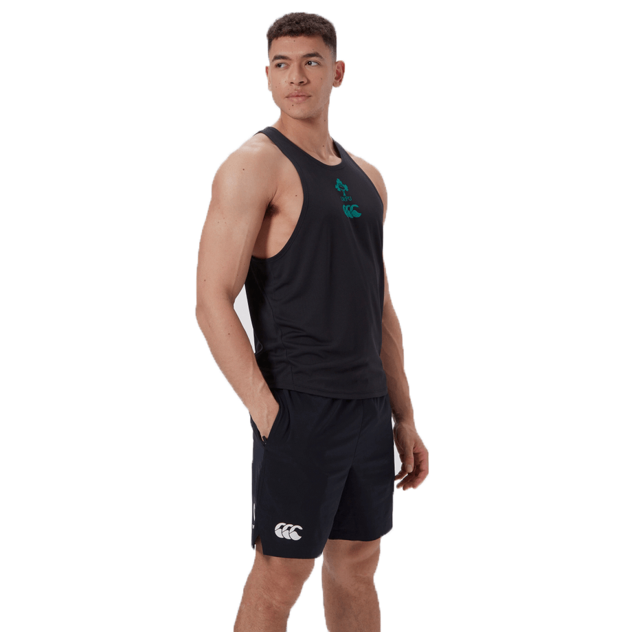 Wearing a black athletic tank top, akin to the Ireland 24 Poly Training Singlet by Canterbury, a person stands with arms relaxed, gazing sideways against a plain backdrop. The quick-drying fabric blends comfort with style effortlessly.