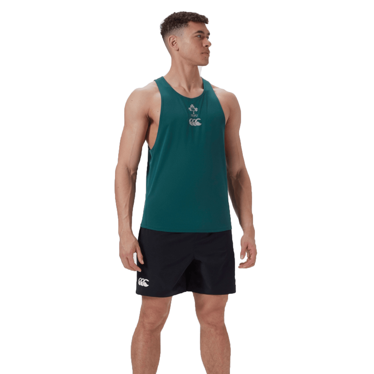 On a white background, a man stands with arms by his sides wearing the Ireland 24 Poly Training Singlet by Canterbury. The green sleeveless top with a clover design and quick-drying fabric is paired with black shorts, ideal for any setting.