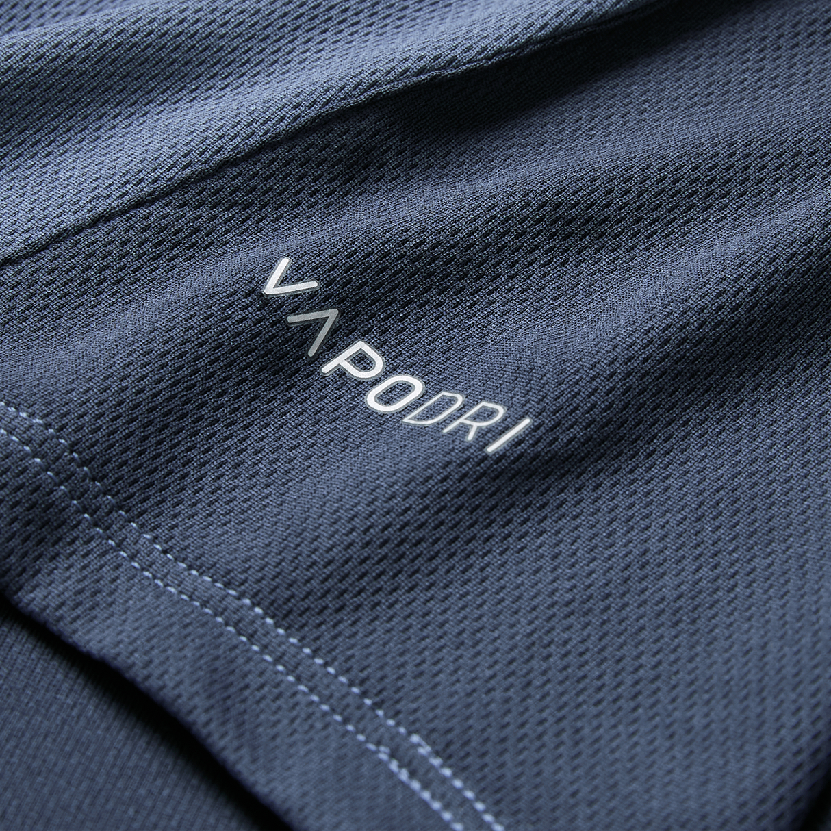 Close-up of dark blue textured fabric from the Ireland 26/27 Summer Tour Superlight Training Singlet by Canterbury, featuring "VAPODRI" in white and light blue stitching along the seam.
