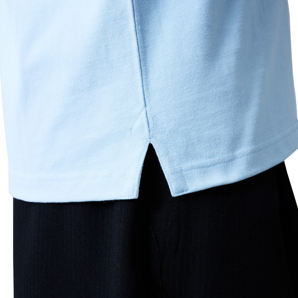 Close-up of the lower hem of the Canterbury Solid Dye Rugby Jersey by Canterbury in light blue, featuring a center split, worn over black pants.