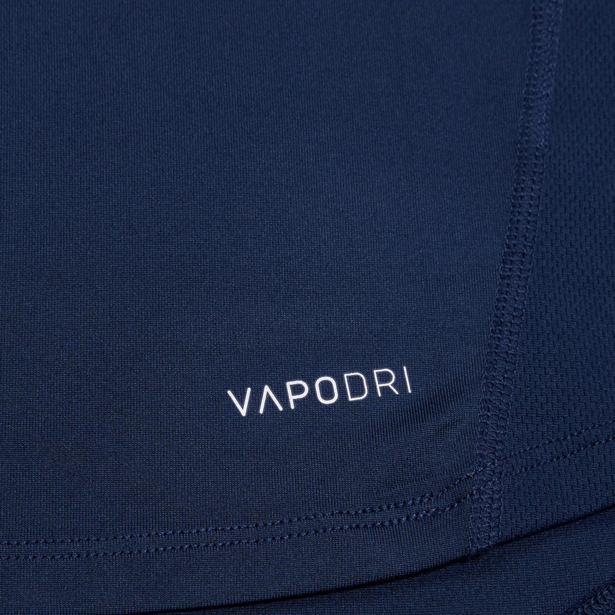 Close-up of navy blue Canterbury Large Logo Superlight Tee AM fabric with "VAPODRI" in white, showing stitching and texture details on this lightweight Canterbury performance shirt.