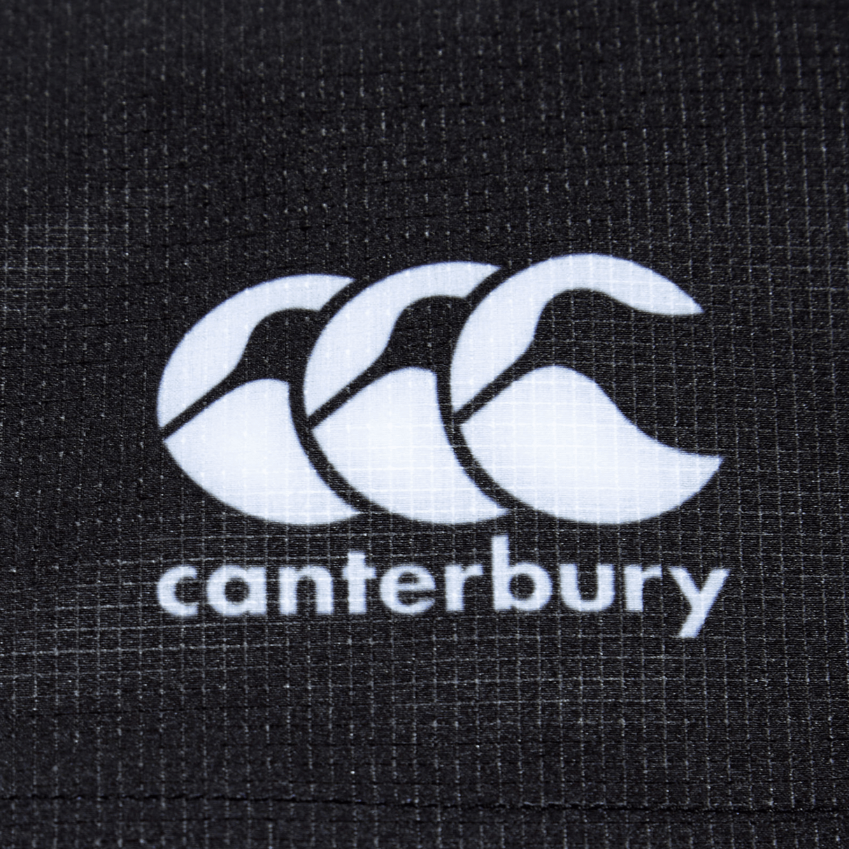 Close-up of the Bundle Canterbury logo on a textured black fabric background, showcasing the durable fabric of the Women's Canterbury Yokohama Short 3-Pack Bundle.