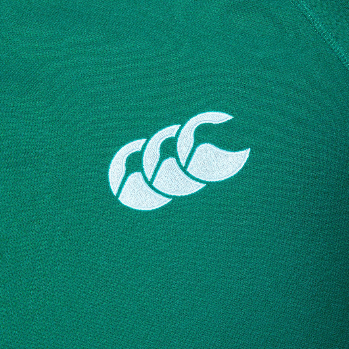 A close-up of the Ireland 25/26 Long Sleeve Classic Home Jersey by Canterbury shows a green fabric with a white logo featuring three overlapping curved shapes, capturing the iconic design.