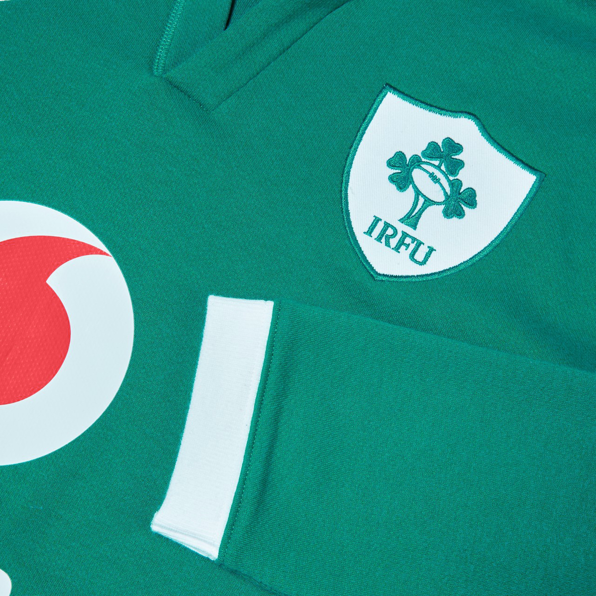 Close-up of the Ireland 25/26 Long Sleeve Classic Home Jersey by Canterbury, showcasing a green design with the IRFU logo—a shamrock and rugby ball—and a hint of red and white circular detail. Ideal for any Irish rugby fan to showcase their pride.