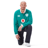 A man smiles proudly in his Ireland 25/26 Long Sleeve Classic Home Jersey by Canterbury, paired with jeans and white shoes against a plain white background.