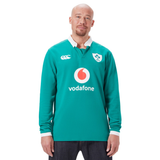 A person proudly wearing the Ireland 25/26 Long Sleeve Classic Home Jersey by Canterbury stands against a crisp white backdrop, showcasing the sponsorship and logo.