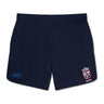 Introducing the Claremont Colleges Elite Woven Short by Canterbury: a pair of navy blue rugby shorts featuring an EMB Canterbury logo on the left leg and a white and red crest on the right leg, perfect for elevating your training experience.