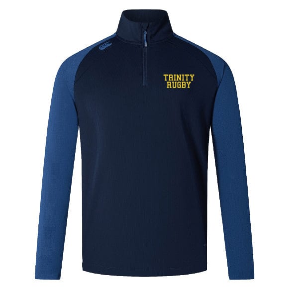 A women's long-sleeve rugby top from EMB Canterbury, the Trinity College Women's Elite First Layer by Canterbury, in navy blue and light blue with "TRINITY RUGBY" text in yellow on the left chest, features VapoDri technology for superior moisture-wicking performance.