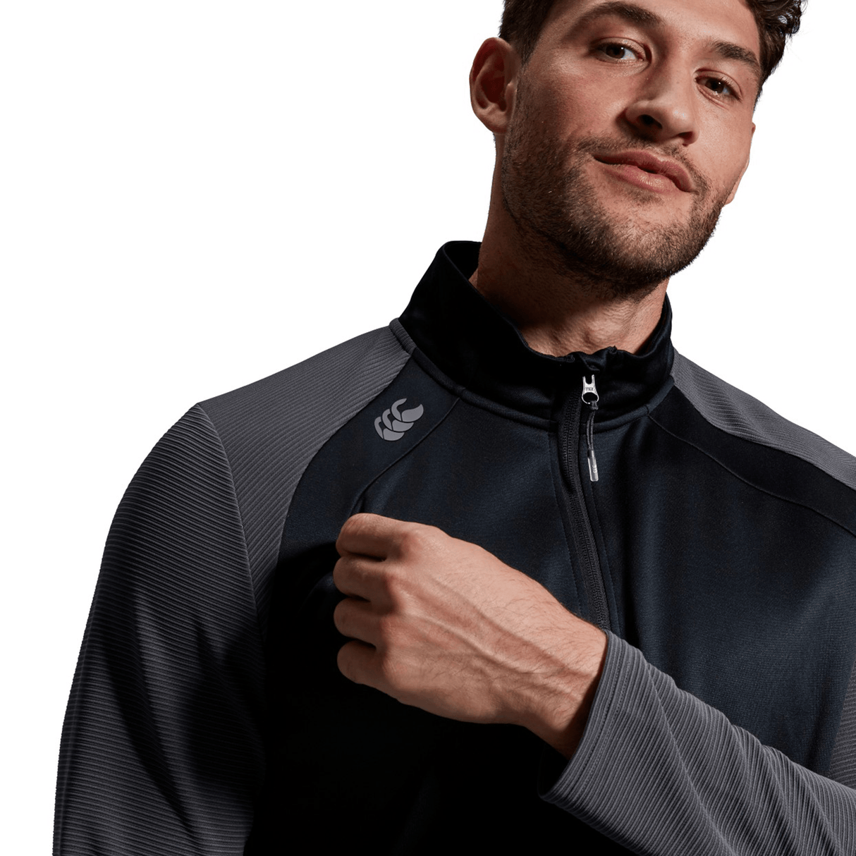 Man in a grey Canterbury Elite 1/4 Zip Top jacket looking off to the side, with a stylized logo on the chest, set against a white background.