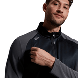 Man in a grey Canterbury Elite 1/4 Zip Top jacket looking off to the side, with a stylized logo on the chest, set against a white background.