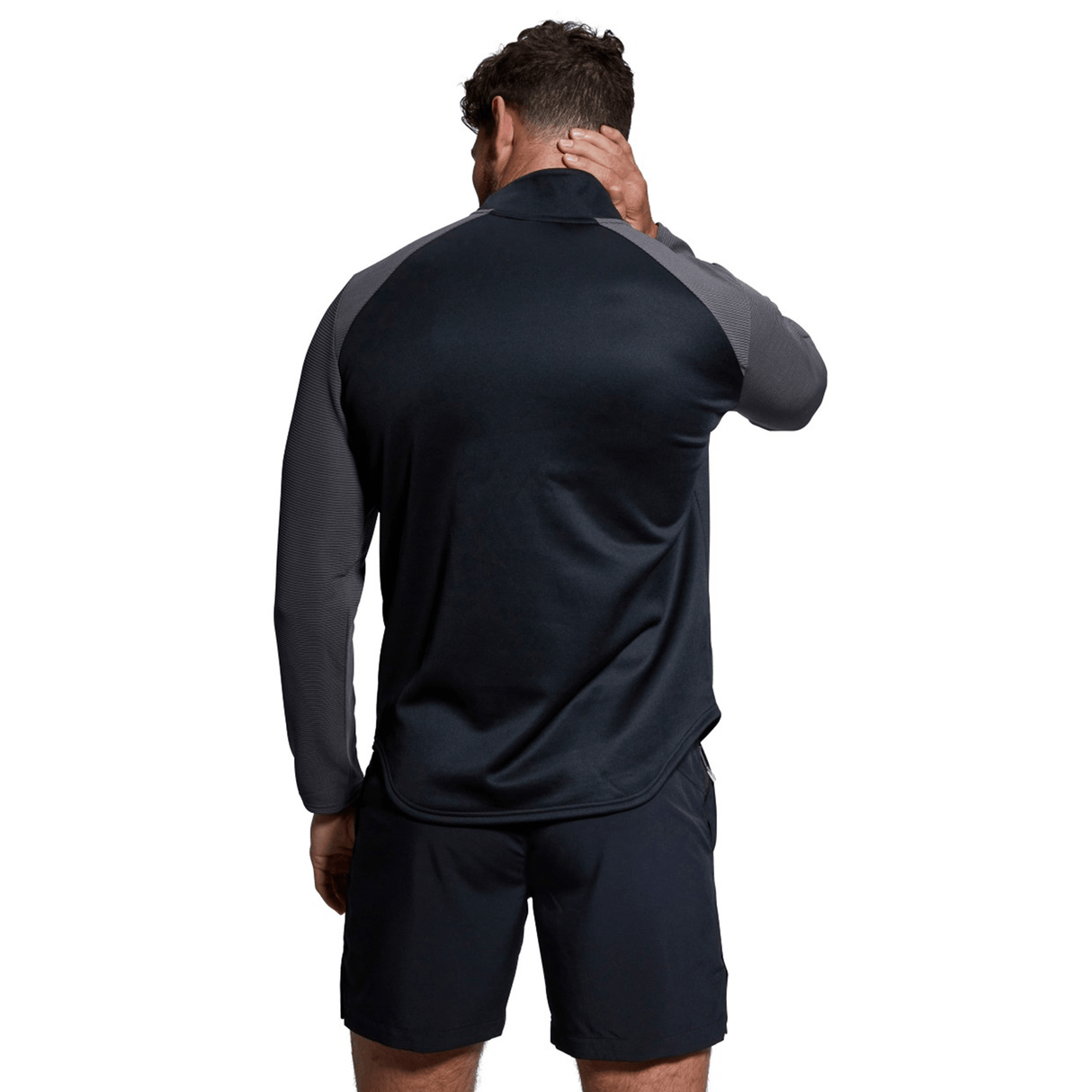 Man seen from behind wearing a Canterbury Elite 1/4 Zip Top dark long-sleeve shirt and black shorts, touching his neck, isolated on a white background.