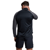 Man seen from behind wearing a Canterbury Elite 1/4 Zip Top dark long-sleeve shirt and black shorts, touching his neck, isolated on a white background.