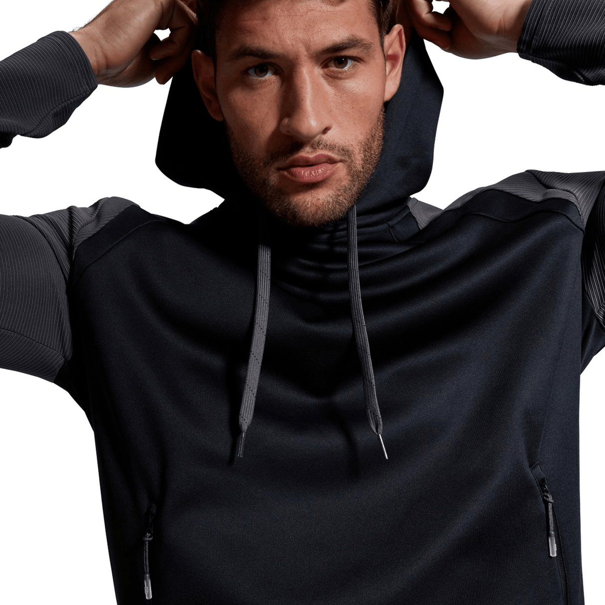A man wearing a Canterbury Elite Training Hoodie made from premium fabrics looks directly at the camera, gripping the hood with both hands.
