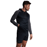 A man in a dark navy and gray Canterbury Elite Training Hoodie made from premium fabrics, paired with black shorts, stands with his left hand in his pocket, looking to the side.