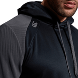 A person wearing a Canterbury Elite Training Hoodie with textured shoulders and drawstrings. The premium fabrics enhance the comfortable and versatile design, though the upper part of their face is not visible in the close-up shot.