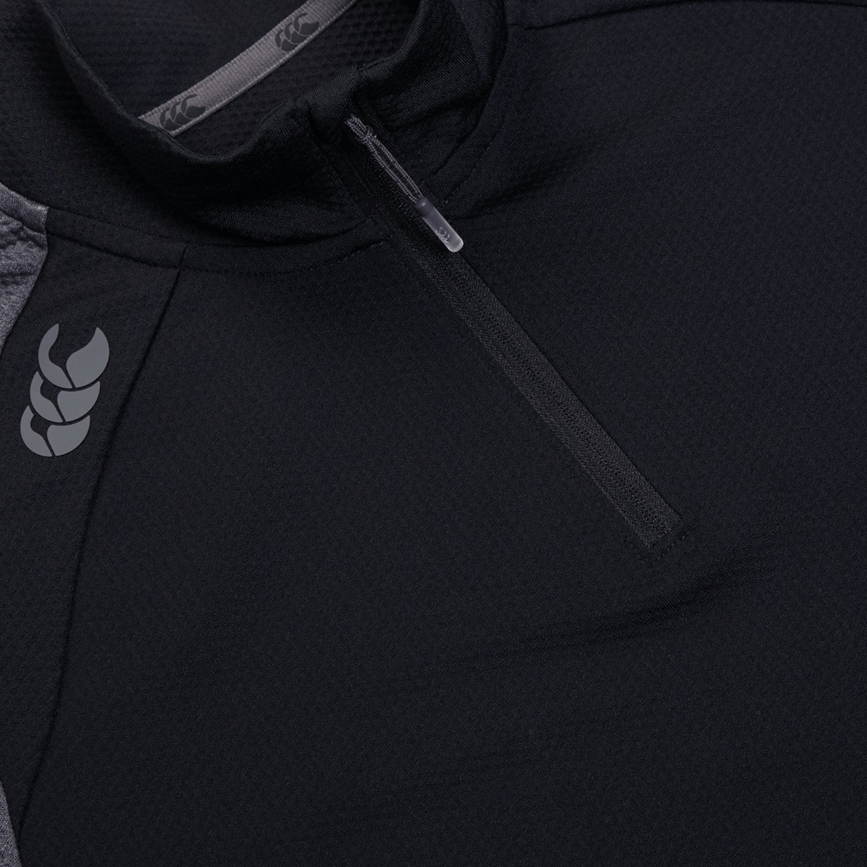 Close-up of a black Canterbury Women's Elite First Layer quarter-zip jacket, featuring VapoDri technology, a subtle shoulder logo, and an intricate honeycomb pattern.