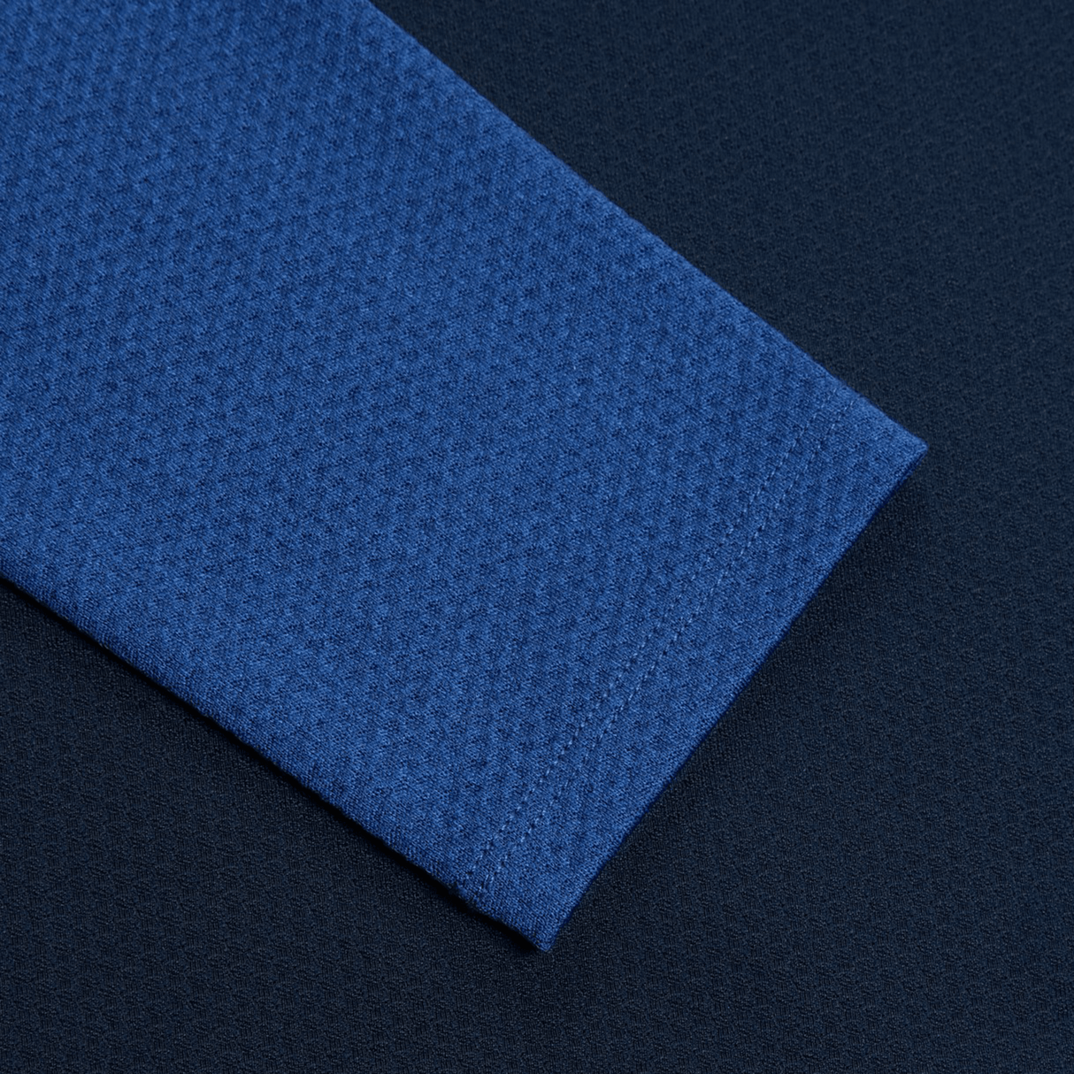 Close-up of the Women's Canterbury Elite First Layer, featuring a blue honeycomb fabric overlapping a dark blue textured background, highlighting its intricate design.