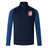 The Montgomery Bucks Griffins Elite First Layer by EMB Canterbury is a navy and blue long-sleeve rugby top with a quarter-zip, white lion crest, "MERIT" on the left chest, VapoDri tech, and a small logo on the right shoulder.