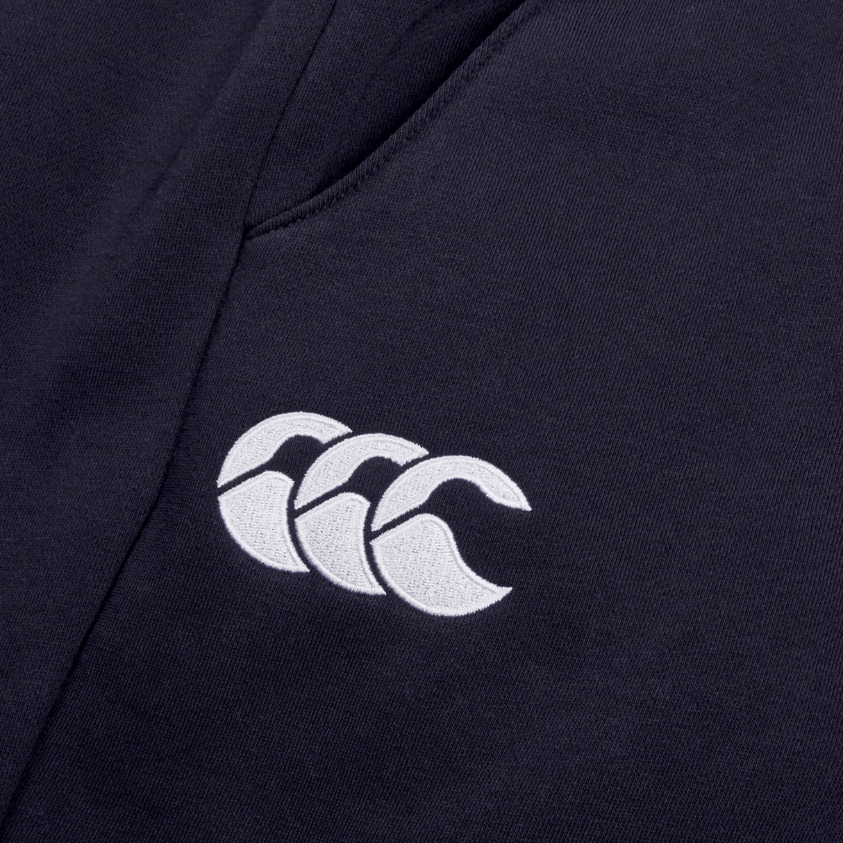 Close-up of a dark fabric with a white Canterbury logo featuring three overlapping curved shapes, crafted from cotton blend fleece on Women's Leisure Sweatpants by Canterbury.