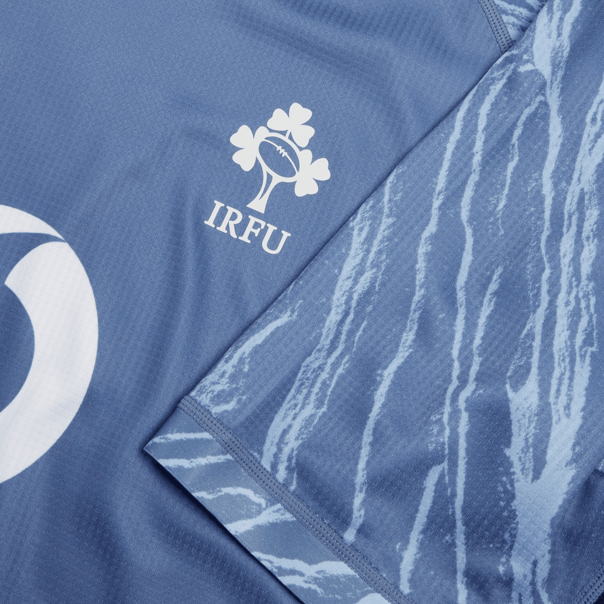 Close-up of the Ireland 24 Training Pro Jersey by Canterbury, a blue sports jersey by Canterbury featuring the IRFU logo and a design resembling tree bark on one sleeve.