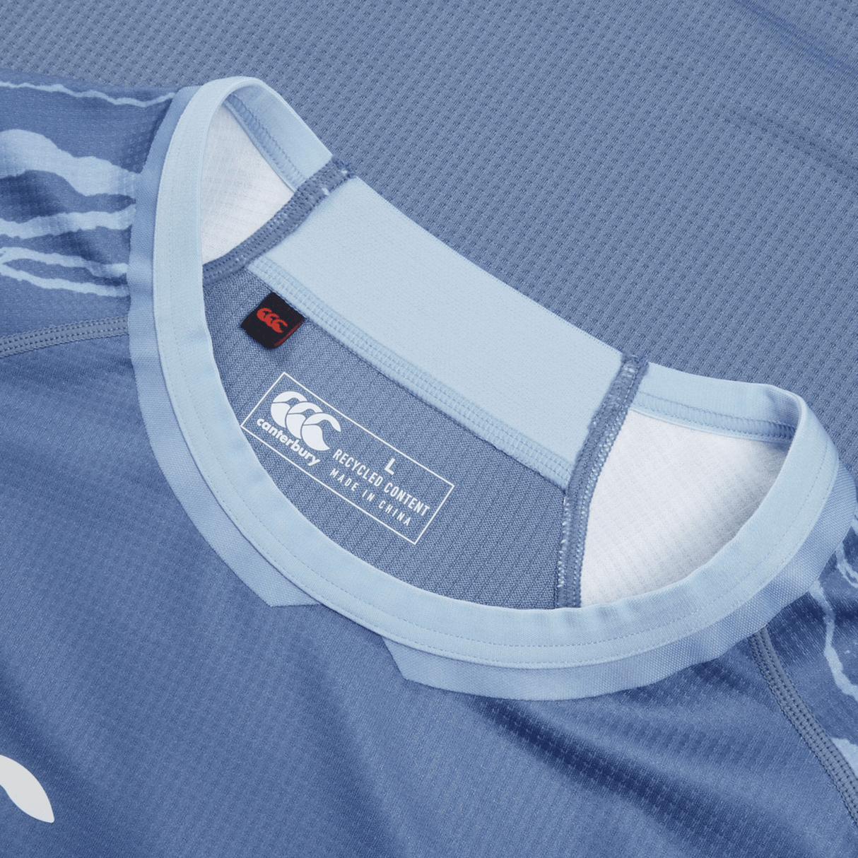 Close-up of a blue sports jersey collar with a Canterbury brand label indicating it is a size large made with recycled content, resembling the Ireland 24 Training Pro Jersey by Canterbury.