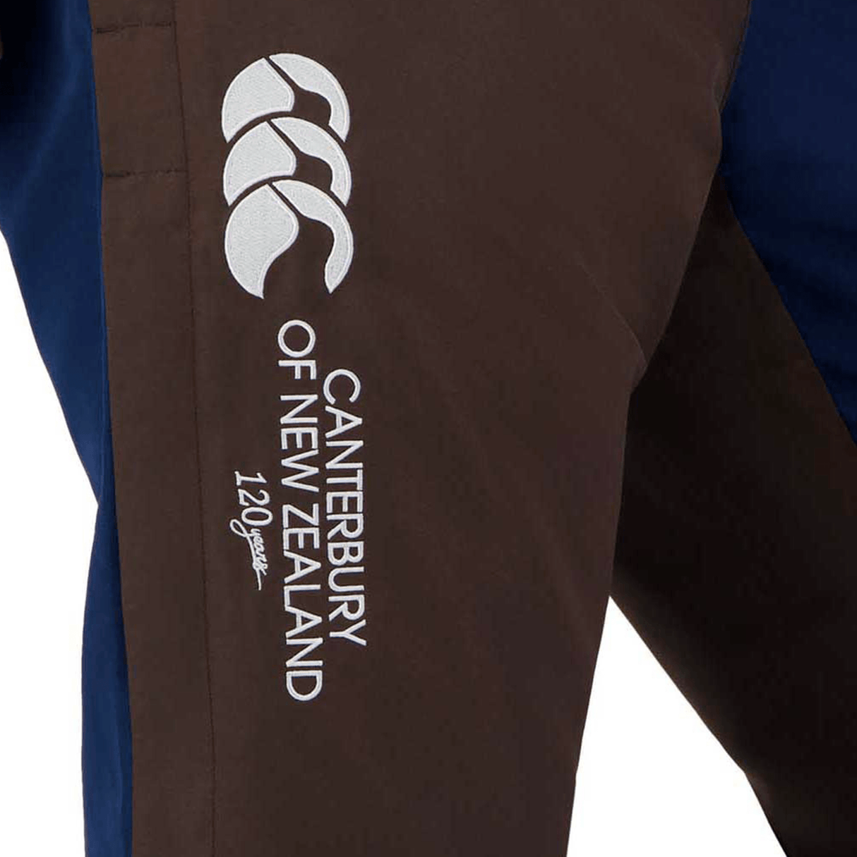 Close-up of the Canterbury Harlequin Block Stadium Trackpant in brown, featuring the Canterbury logo and "Canterbury of New Zealand 120 years" text in white stitching, reminiscent of the iconic Canterbury track pants.