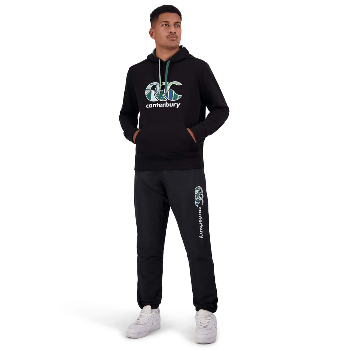 Person in a black Canterbury hoodie and Canterbury Uglies Stadium Pants with a tapered leg, hands in pockets, standing against a white background.