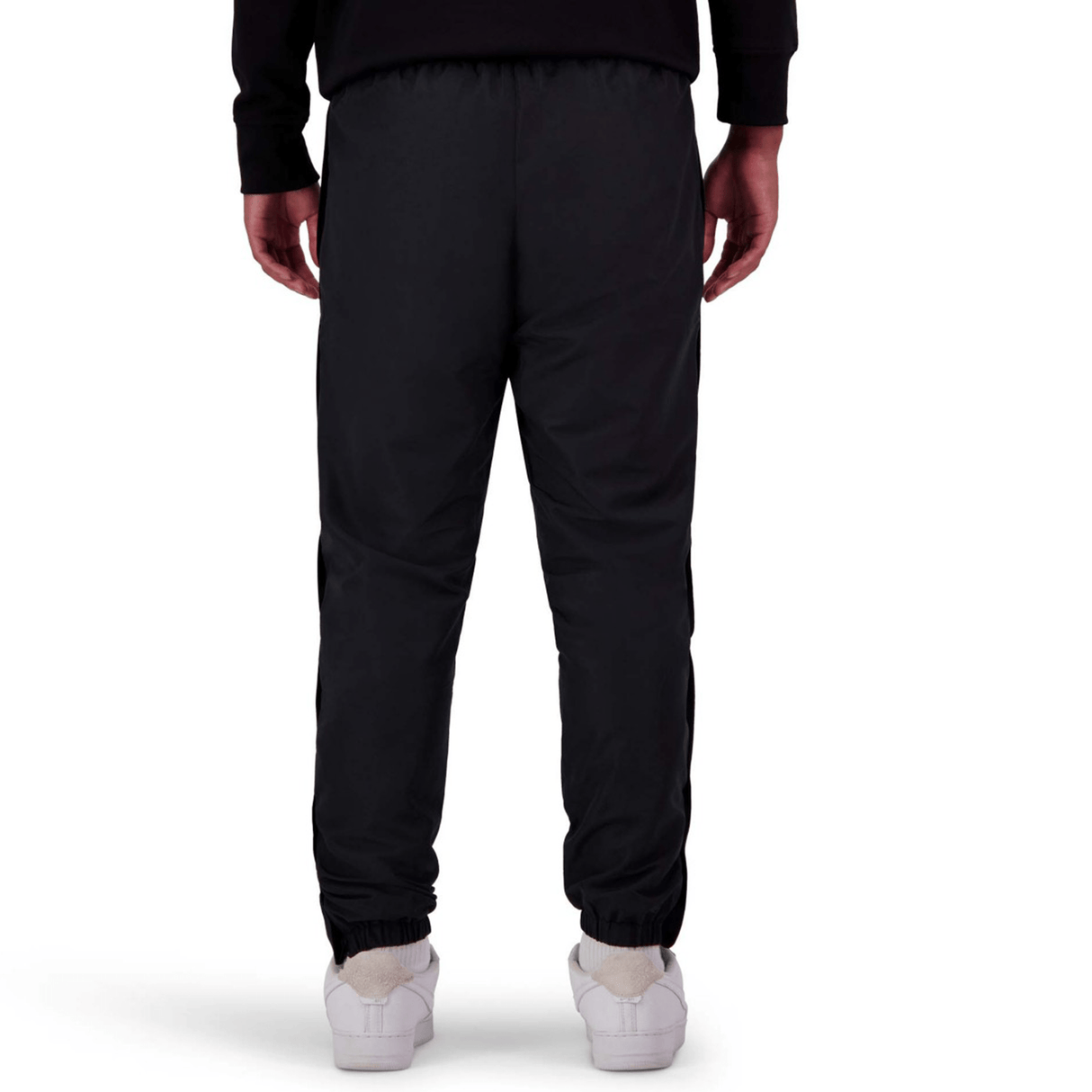 A person standing, viewed from the back, wearing black Canterbury Uglies Stadium Pants by Canterbury with a tapered leg, paired with a black top and white shoes.