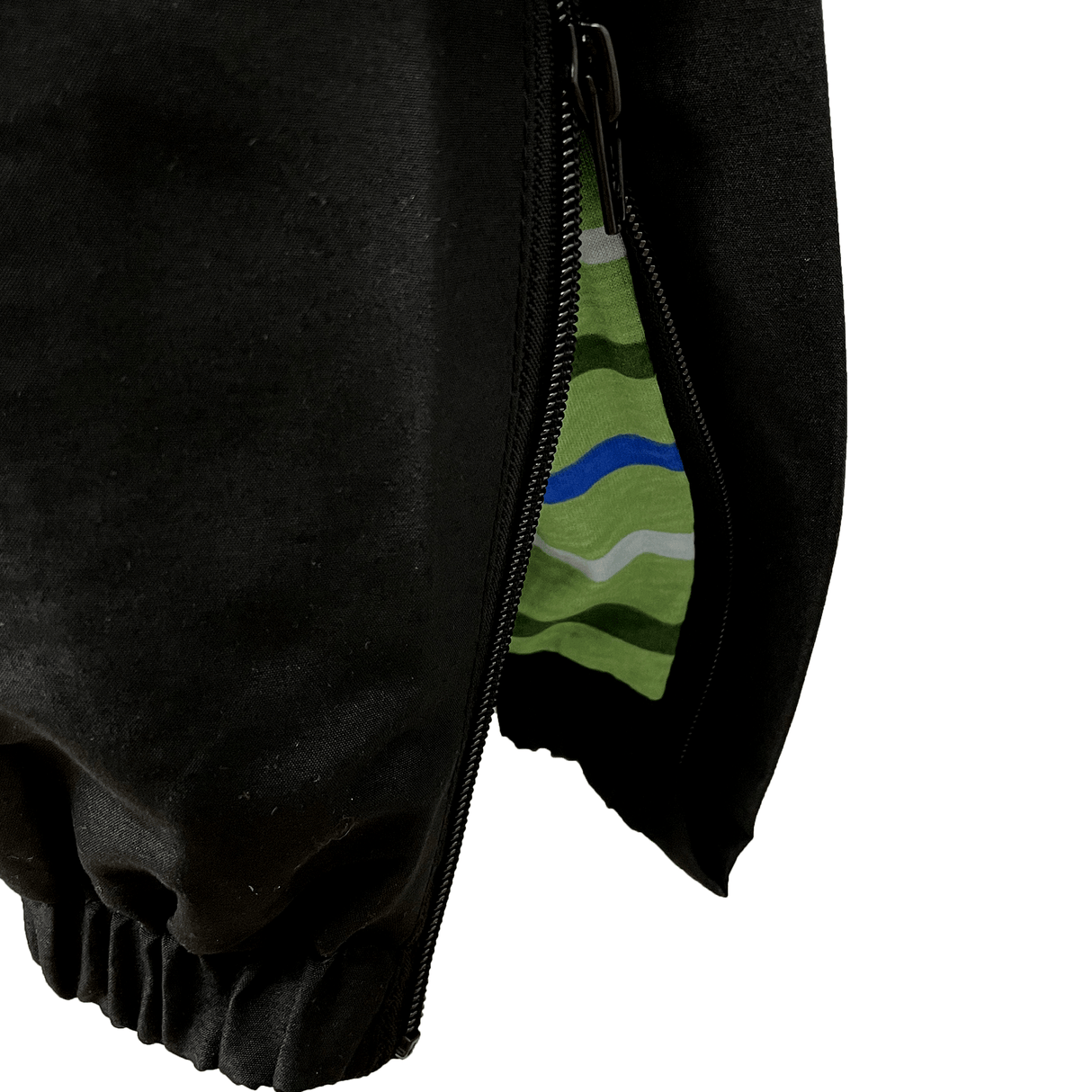 Close-up of a black jacket with an open zipper, unveiling an inner lining adorned with green, blue, and grey stripes. An elastic cuff at the bottom is prominently visible, a detail reminiscent of what you'd find on Canterbury's Uglies Stadium Pants.