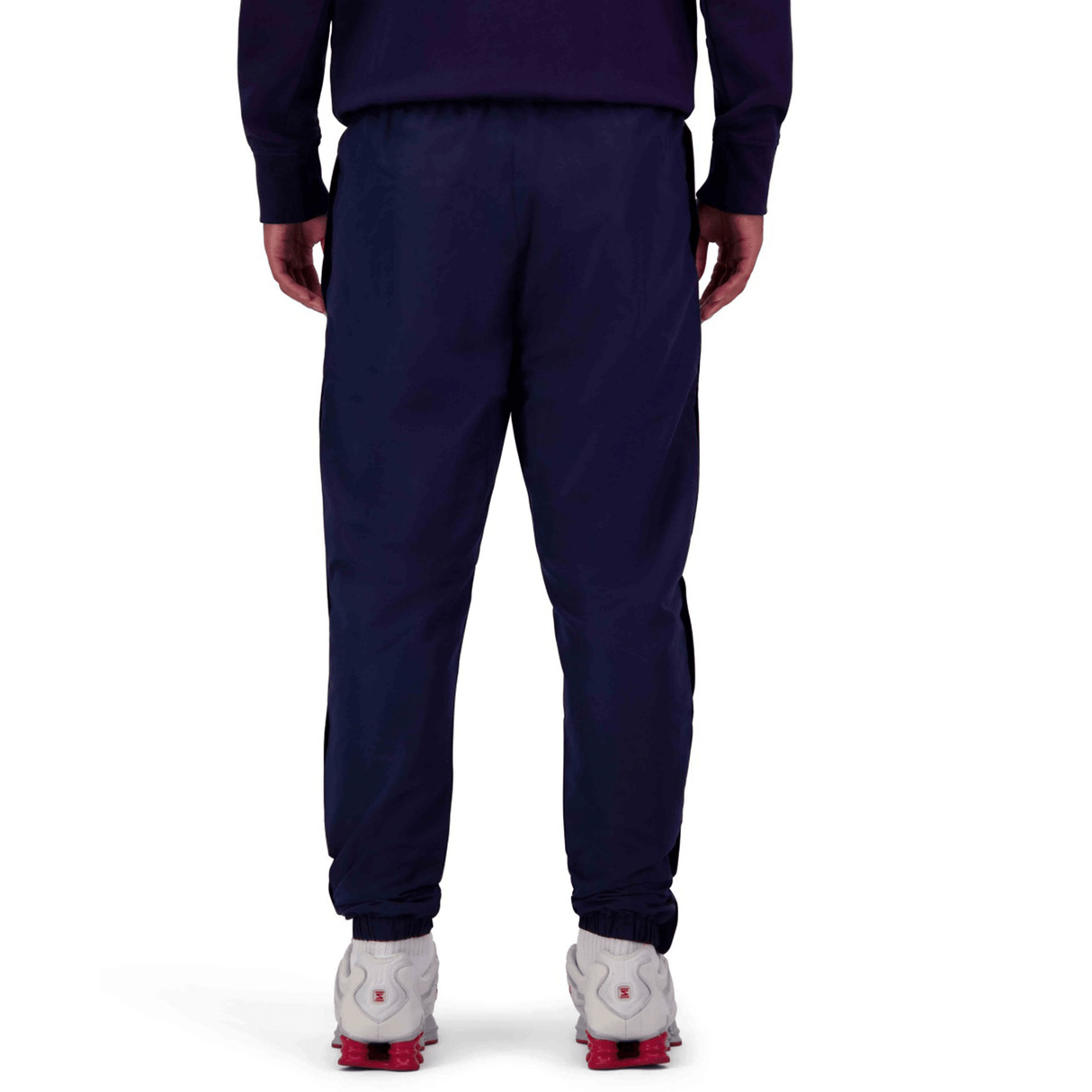 Back view of a person wearing Canterbury Uglies Stadium Pants with a tapered leg and white athletic shoes with red details, standing on a white background.