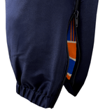 Close-up view of Canterbury's Uglies Stadium Pants, showcasing their tapered leg design and open zippered pocket, which reveals a lining accented with orange, blue, and white stripes in a stylish navy blue color.